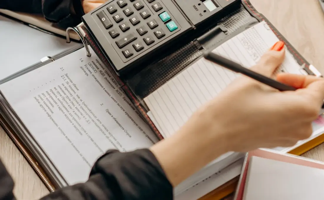 Pessoa confere documentos e usa uma calculadora para revisar uma dívida empresarial