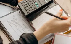 Pessoa confere documentos e usa uma calculadora para revisar uma dívida empresarial