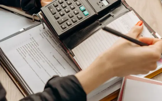 Pessoa confere documentos e usa uma calculadora para revisar uma dívida empresarial
