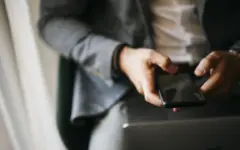 Pessoa usando celular ao lado de um notebook para consultar informações financeiras
