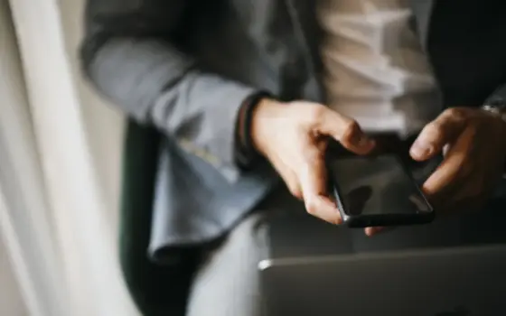 Pessoa usando celular ao lado de um notebook para consultar informações financeiras