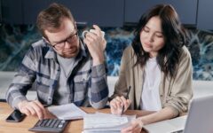 Casal confere contas e orçamento com calculadora e notebook à mesa da cozinha