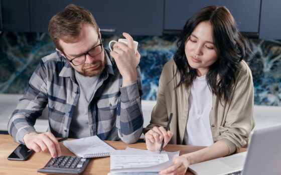 Casal confere contas e orçamento com calculadora e notebook à mesa da cozinha
