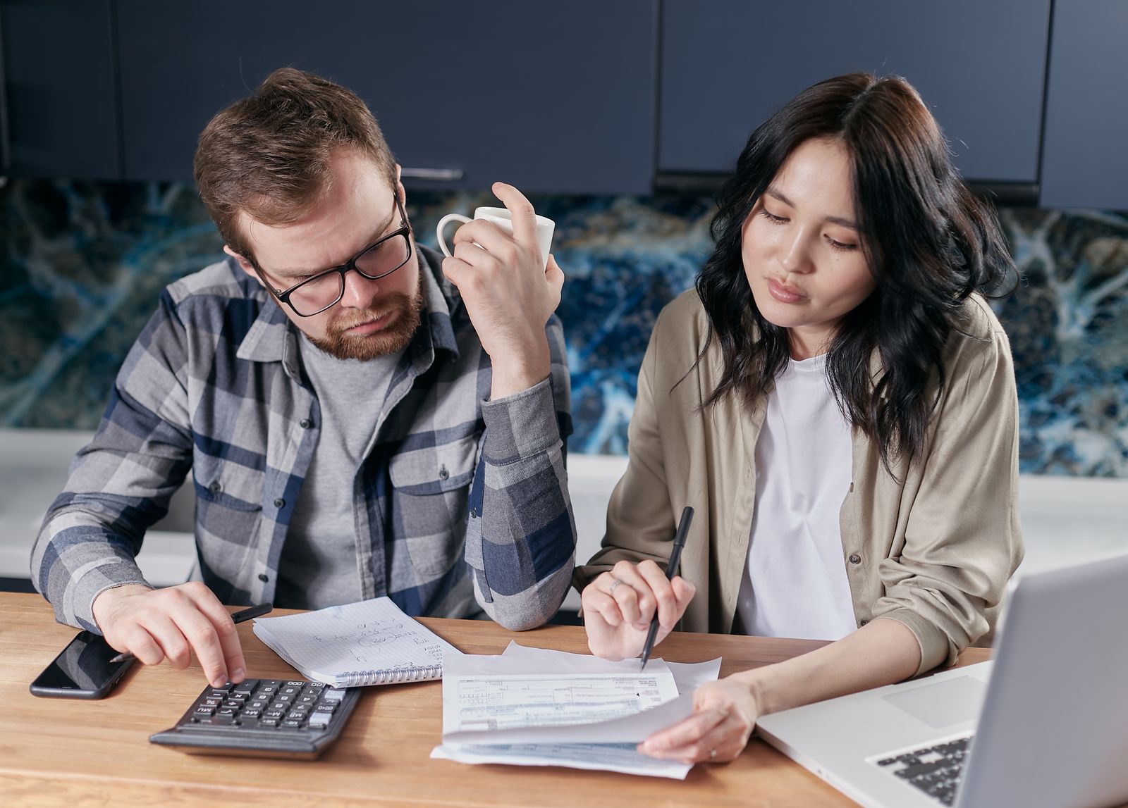 Casal confere contas e orçamento com calculadora e notebook à mesa da cozinha