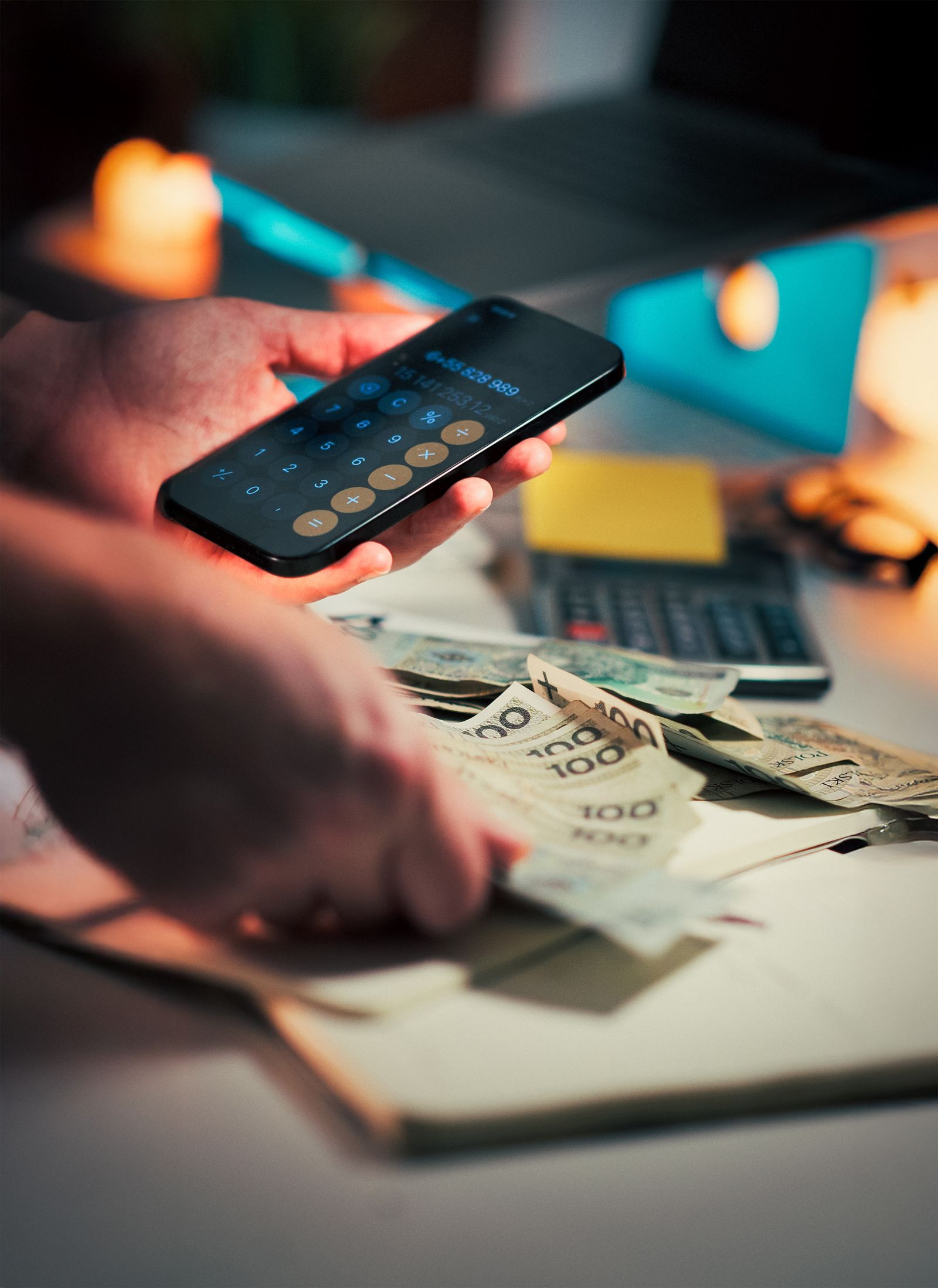 Pessoa calcula uma dívida no celular ao lado de dinheiro e caderno sobre uma mesa
