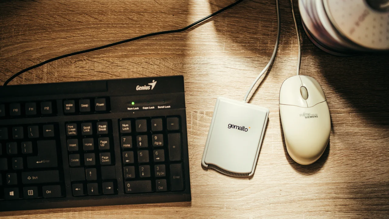 Teclado, mouse e leitor de cartões sobre mesa de trabalho