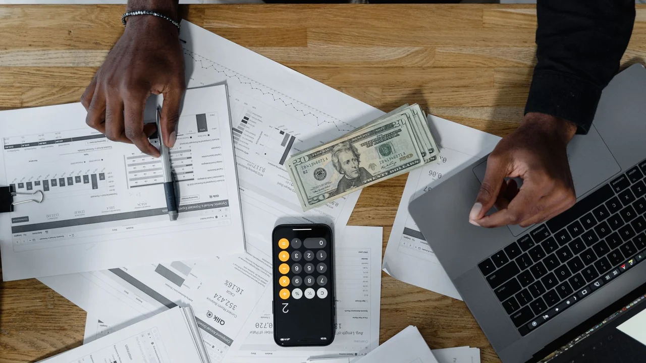 Documentos, calculadora e computador sobre uma mesa usados na conferência de uma dívida empresarial