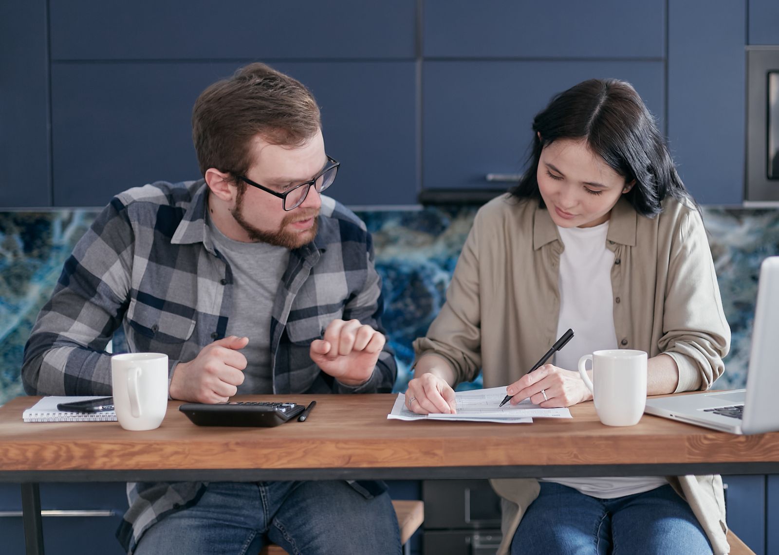 Duas pessoas analisam documentos financeiros com notebook e calculadora em uma mesa