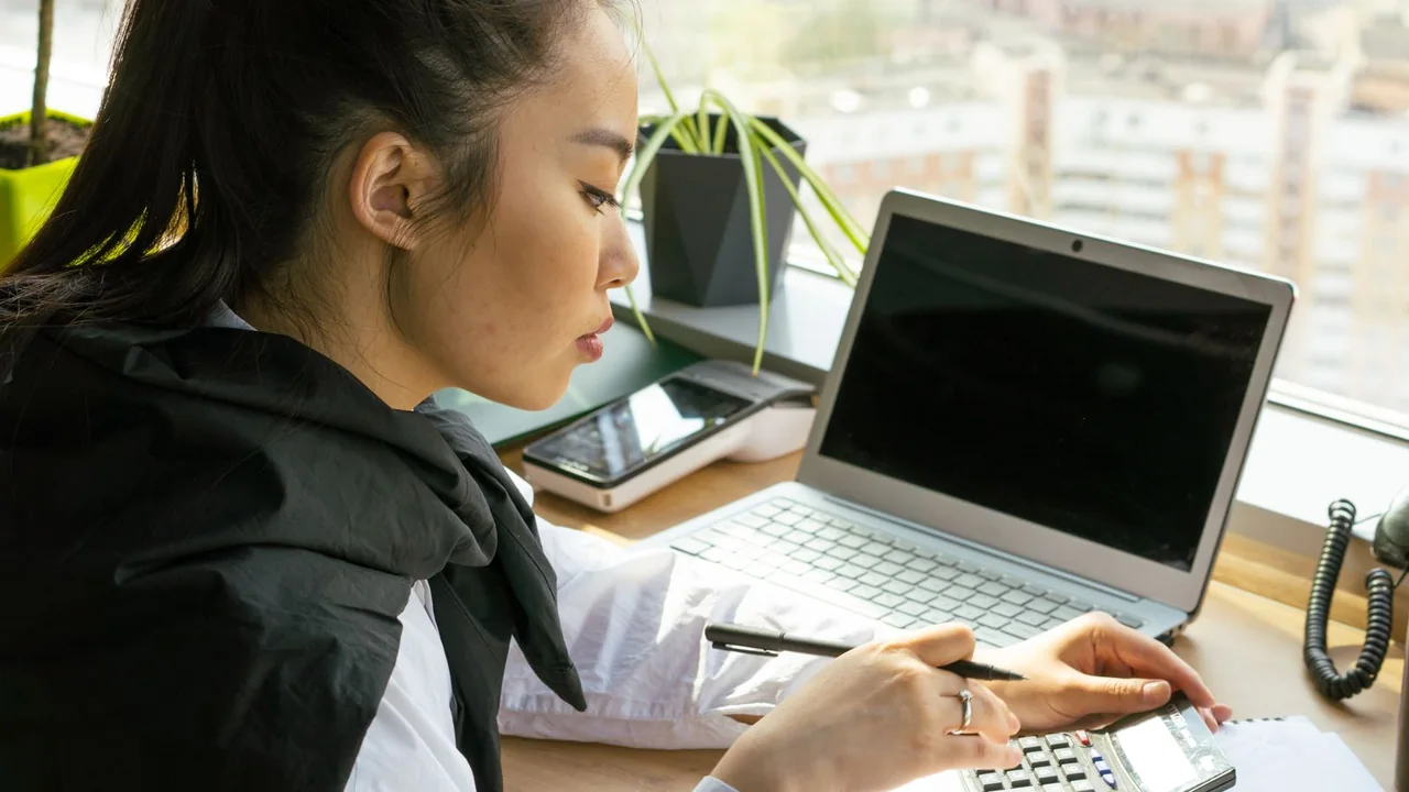 Empreendedora usa calculadora ao lado do computador para acompanhar as finanças do negócio