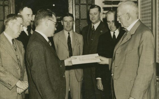 Duas pessoas apresentam documentos de propriedade e um cheque durante a entrega de uma casa em Brisbane, em registro histórico