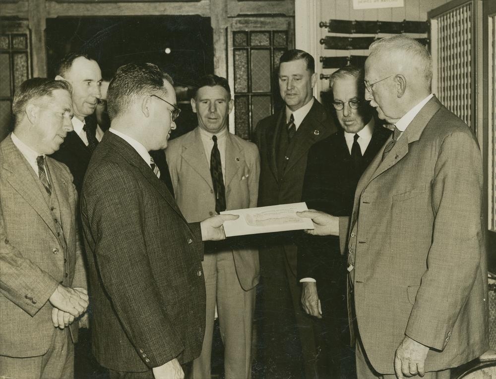 Duas pessoas apresentam documentos de propriedade e um cheque durante a entrega de uma casa em Brisbane, em registro histórico