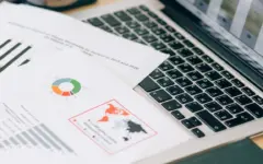 Imagem de documentos e um notebook em uma mesa de trabalho, representando a consulta de editais e intimações fiscais.