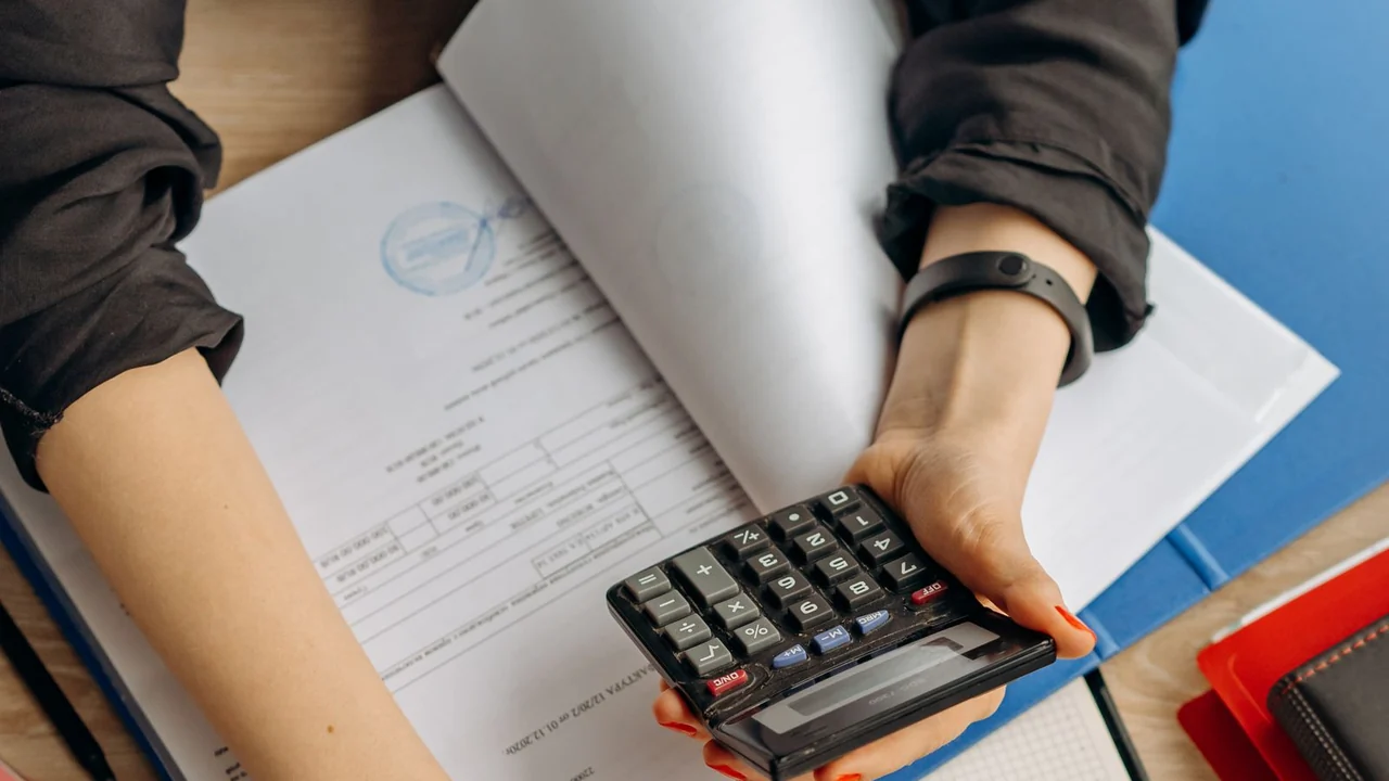 Profissional confere documentos e calculadora ao lado de um notebook