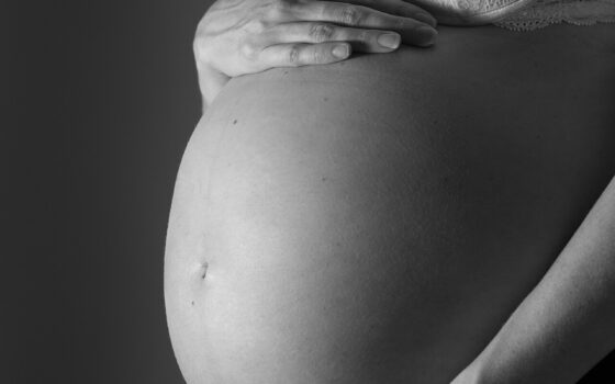 Mulher grávida em terceiro trimestre segura a barriga em close, em fotografia em preto e branco