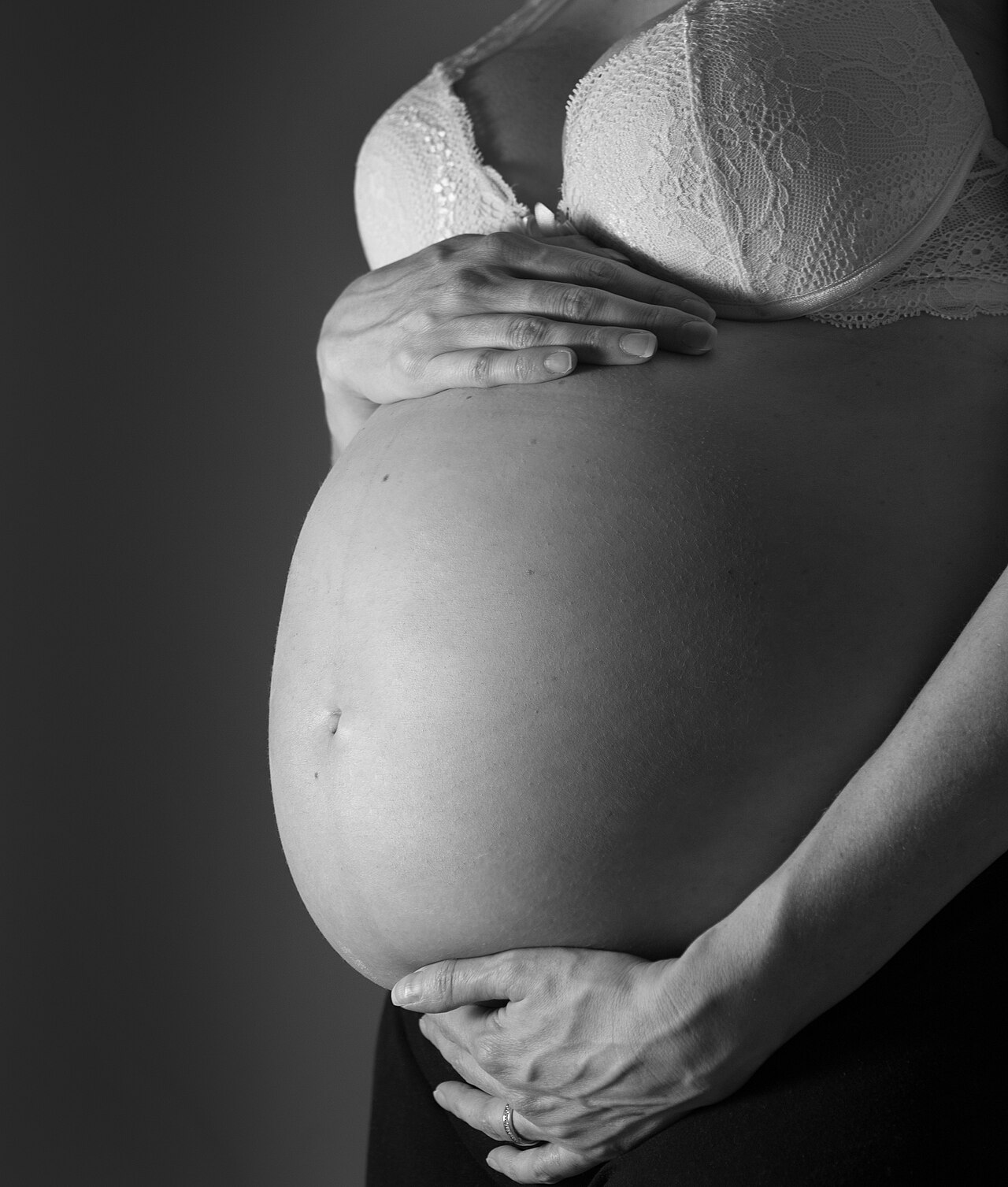 Mulher grávida em terceiro trimestre segura a barriga em close, em fotografia em preto e branco