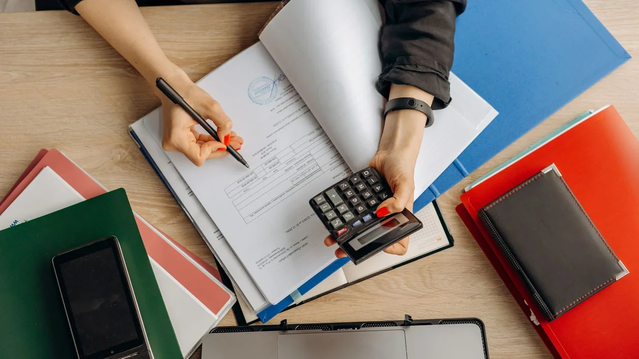 Pessoa confere documentos e calcula despesas de um pequeno negócio em uma mesa de trabalho