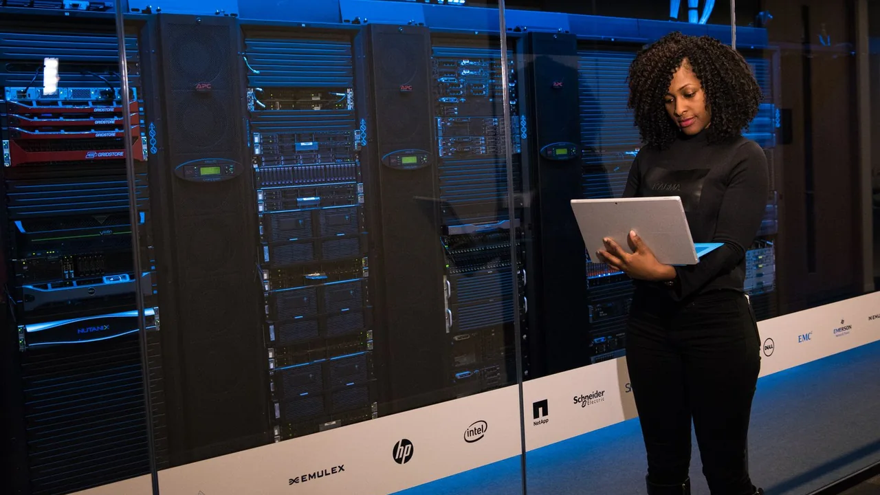 Profissional de tecnologia usa um notebook diante de racks de servidores em um data center.