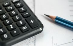 Calculadora, lápis e papéis sobre uma mesa, ilustrando o controle de dívidas de uma empresa.