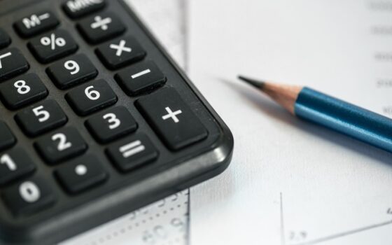 Calculadora, lápis e papéis sobre uma mesa, ilustrando o controle de dívidas de uma empresa.