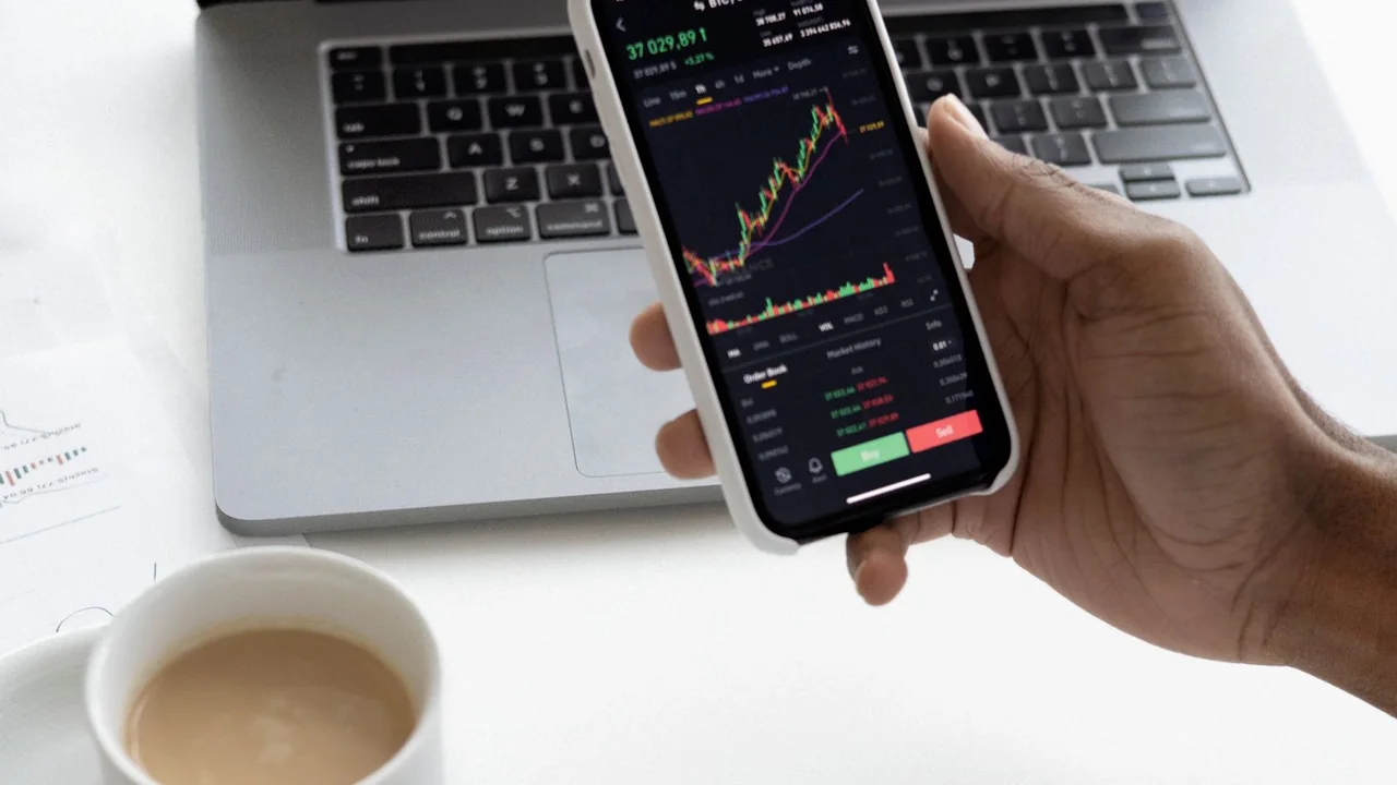 Pessoa usa celular ao lado de notebook, calculadora e documentos para conferir informações financeiras