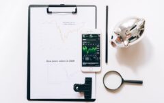 Celular, prancheta, lupa e cofrinho sobre uma mesa, em cena que representa a análise de dados financeiros