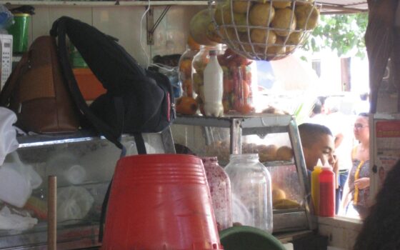 Interior de uma pequena loja de bairro, com prateleiras de produtos e balcão de atendimento.