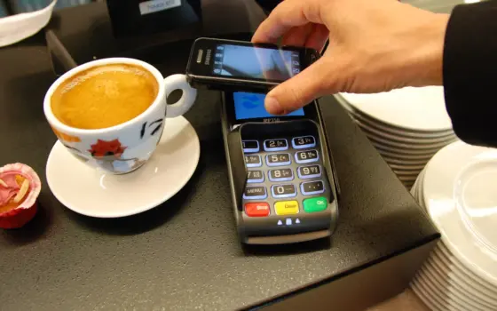 Celular próximo de um terminal de pagamento por aproximação, representando uma compra com Pix e tecnologia NFC.