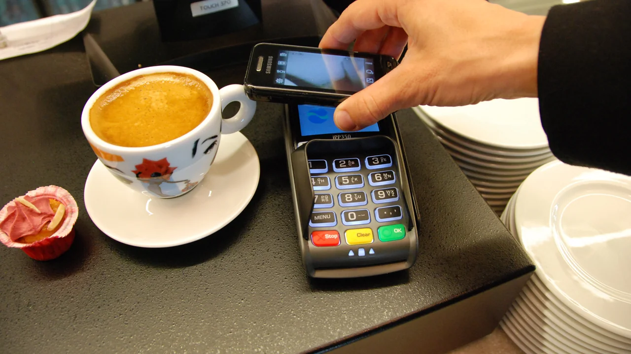 Terminal de pagamento móvel ao lado de uma xícara, representando pagamentos digitais