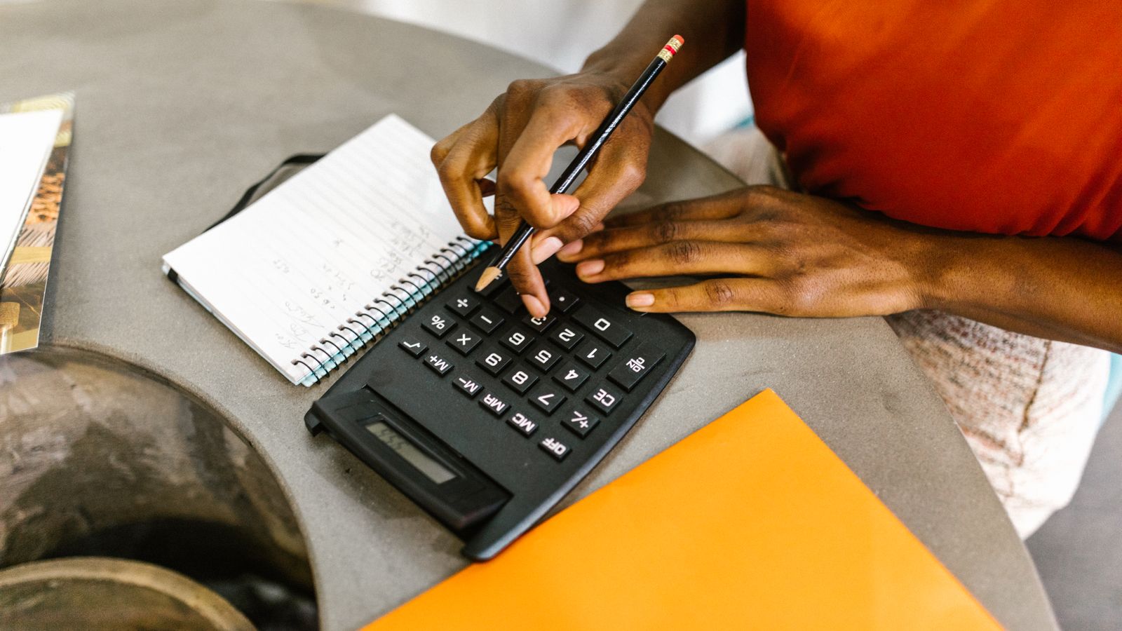 Pessoa usando calculadora e caderno para organizar o orçamento e planejar uma reserva financeira.