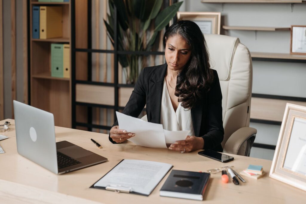Mulher sentada à mesa de escritório analisa documentos impressos, imagem ilustrativa para a organização de informações trabalhistas