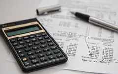Calculadora sobre documentos financeiros em uma mesa, usada para ilustrar a conferência de tributos