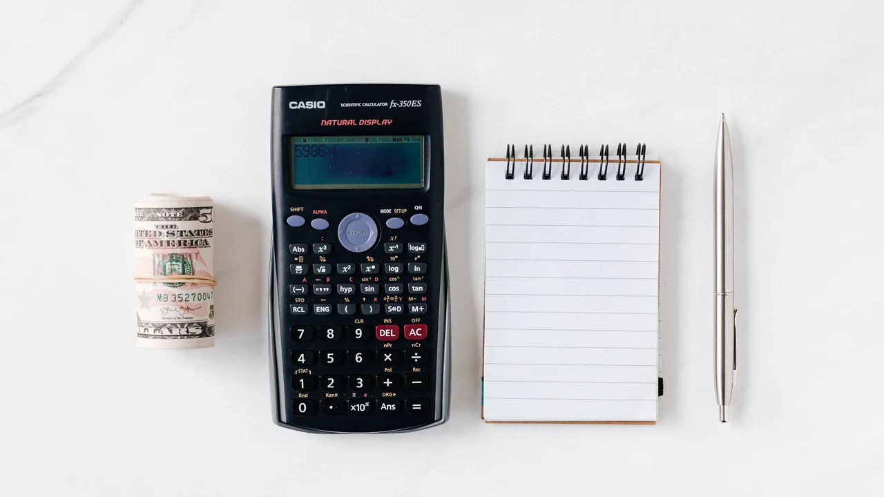 Calculadora, cédulas e caderno usados para fazer contas de orçamento