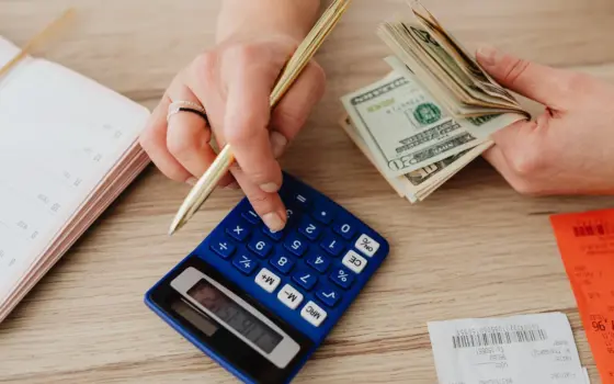 Pessoa organizando dinheiro e contas com calculadora sobre uma mesa