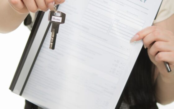 Pessoa segurando chave de imóvel e documento de seguro residencial.