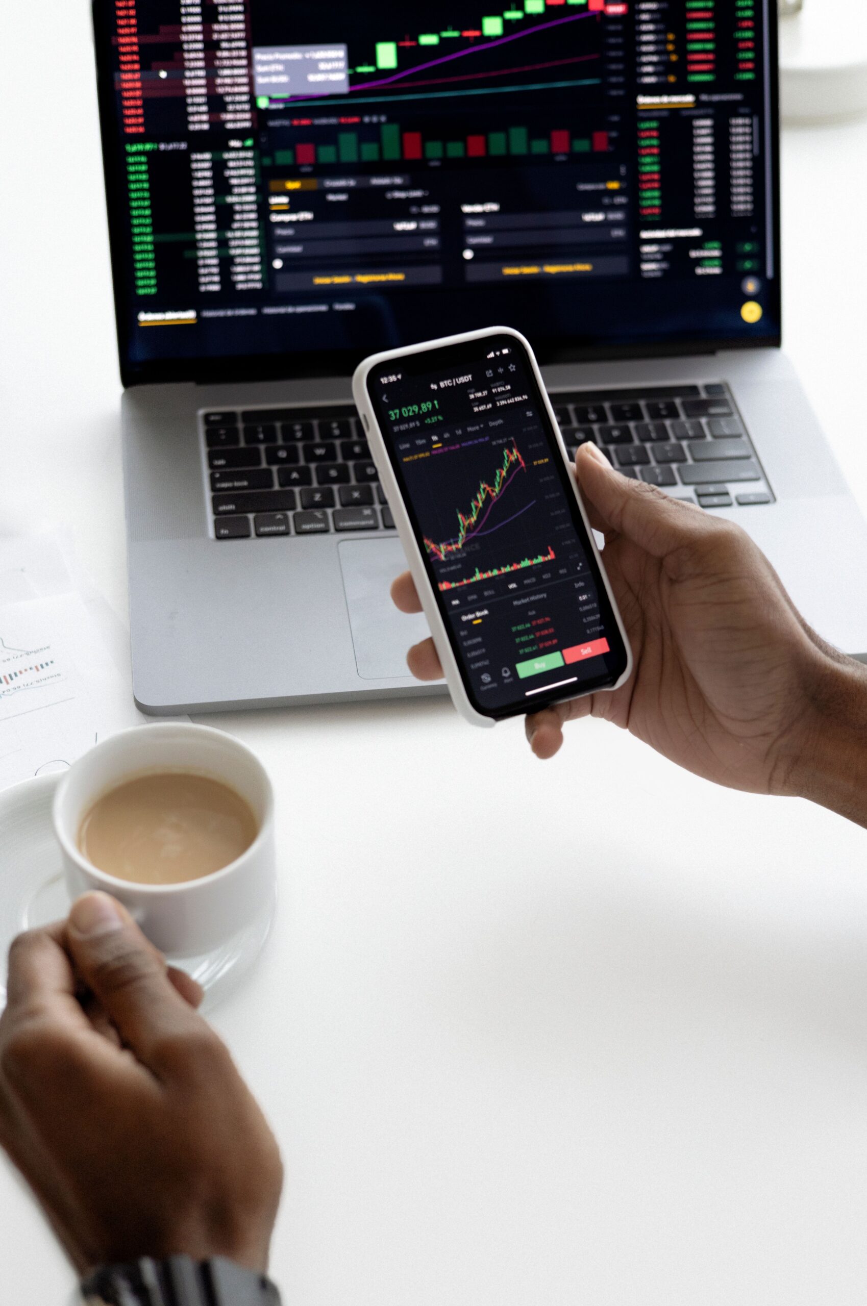 Pessoa analisa gráficos financeiros em um smartphone ao lado de um notebook