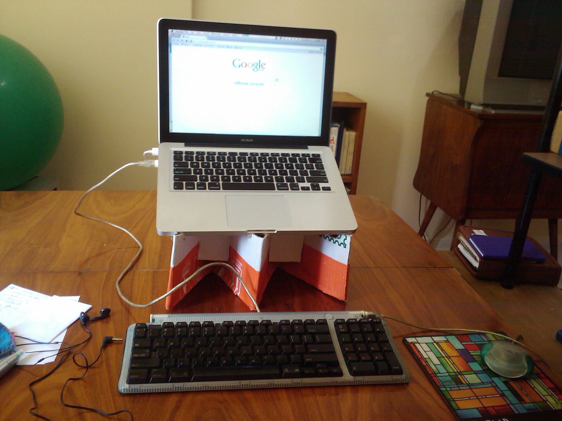 Mesa de trabalho em casa com laptop sobre suporte de papelão e caderno