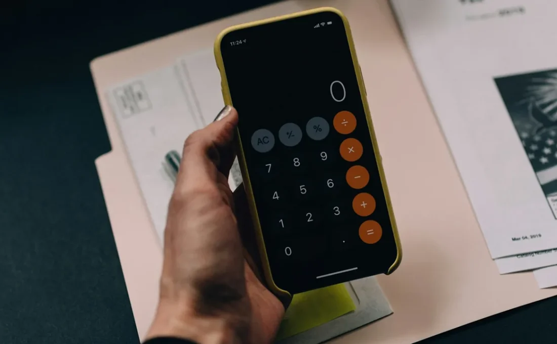 Pessoa calculando despesas com celular e documentos sobre a mesa