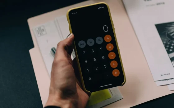 Pessoa calculando despesas com celular e documentos sobre a mesa