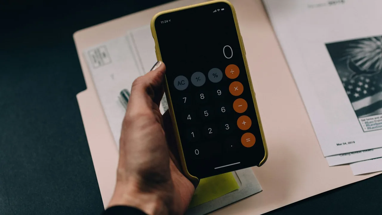 Pessoa usando uma calculadora no celular sobre documentos de planejamento financeiro