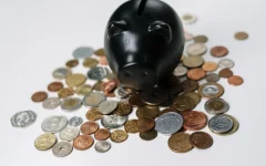 Dinheiro em moedas ao redor de um cofrinho preto, imagem ilustrativa sobre negociação de dívida.