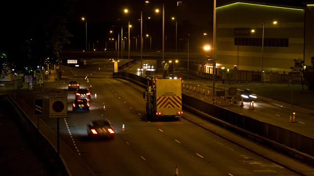 Obra de manutenção viária realizada à noite com iluminação e cones
