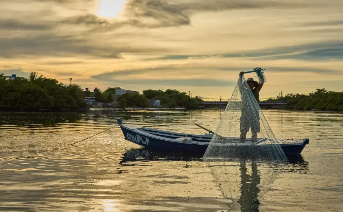 Barco com pescador artesanal lançando rede no rio
