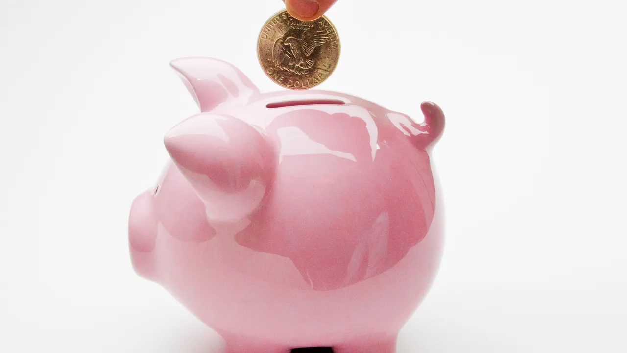 Mão depositando uma moeda em um cofrinho